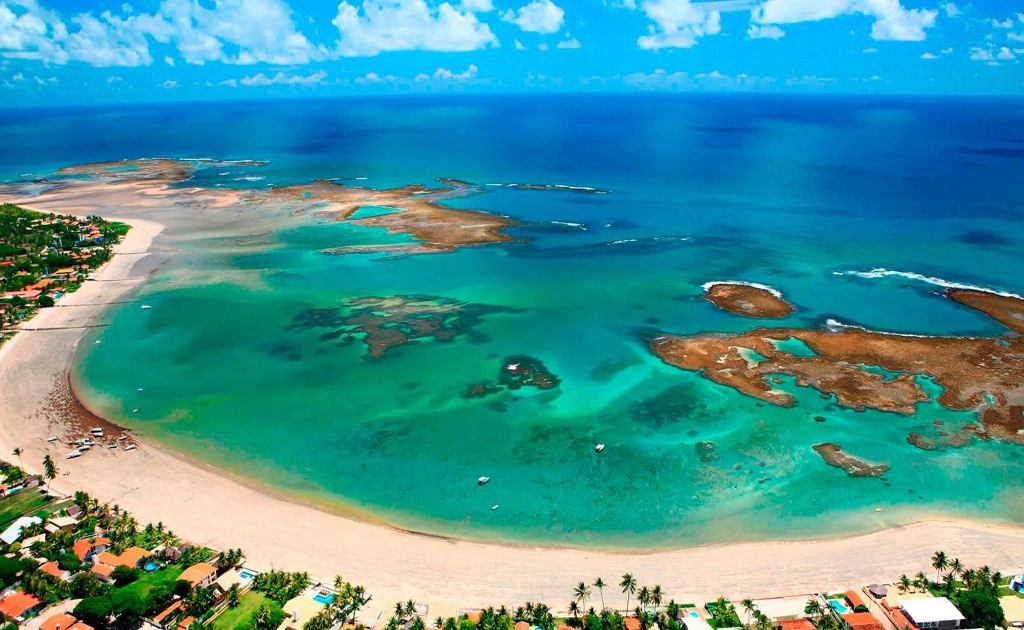 Imagem panorâmica da praia de Porto de Galinhas, com água verde azulada e seus recifes de corais
