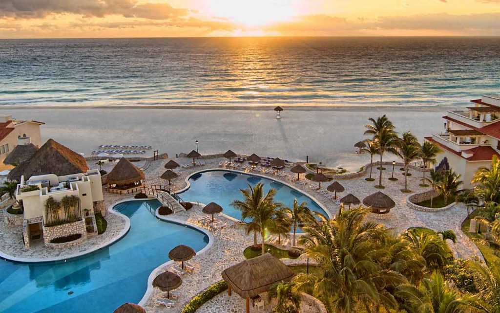 Por do sol na praia de cancun em frente a um hotel.