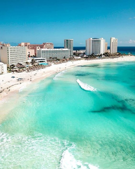 Panorâmica de uma das praias de água azuladas de Cancun, com prédios ao fundo.