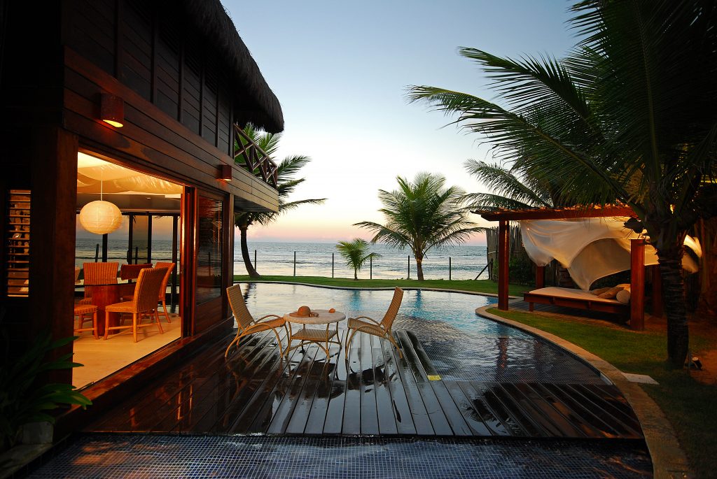 Nos resorts no nordeste, um bangalô de madeira a esquerda, com deck de madeira, cadeiras e um piscina