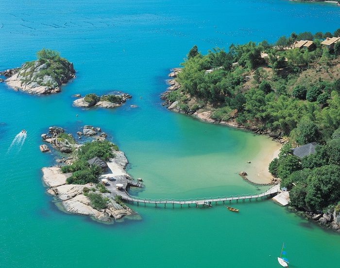 Vista panorâmica de uma pequena ilha ligada ao continente por um  ponte sobre um mar verde e cercado por florestas em hotéis e resorts em santa catarina