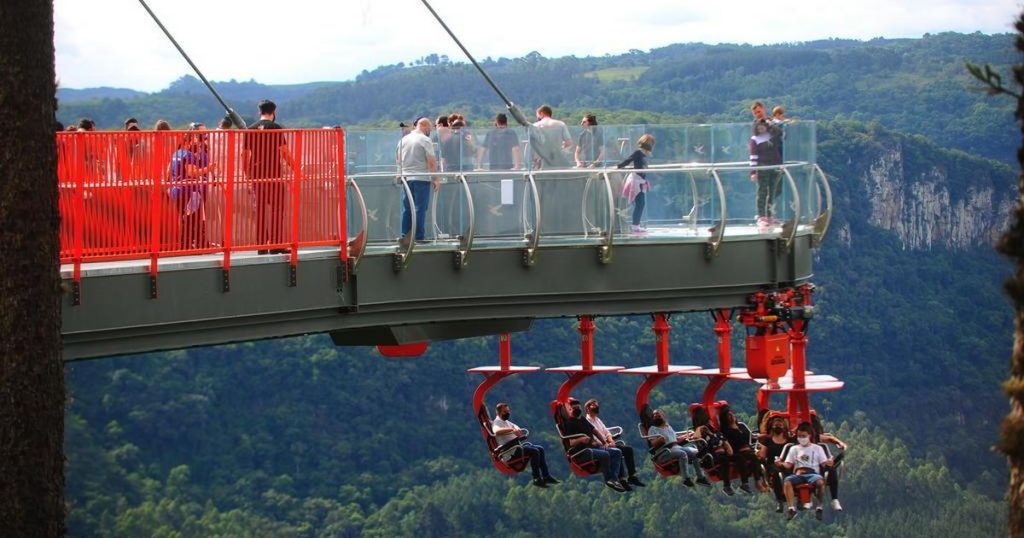 Skyglasse, a plataforma com pessoas observando a vista e, em baixo dela, outras pessoas sentadas em cadeiras especiais em gramado pontos turísticos