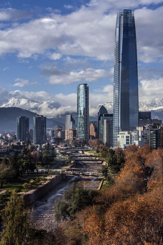 Arranha-céus em meio a uma cidade com áreas verdes e com a cordilheira dos Andes atrás em pontos turísticos no chile