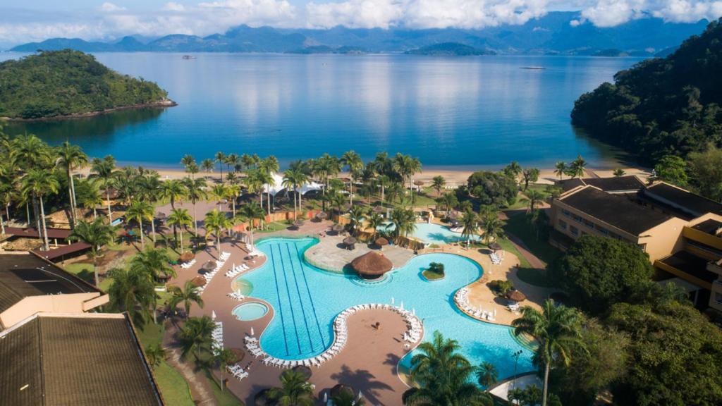 Imagem de cima com um hotel com piscina, seus prédios e sua área de lazer a frente do mar azul, com natureza abundante em hotel em angra dos reis beira mar